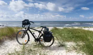 Czarny rower z sakwami na plaży, gotowy do podróży trasą rowerową R10. Morze i niebo w tle.