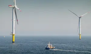 Ogromne turbiny wiatrowe na morzu, symbol nowoczesnej morskiej energetyki wiatrowej, na tle spokojnego oceanu. Statek serwisowy płynie w kierunku jednej z nich.