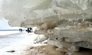 Warstwa lodu na plaży w Mikoszewie, w tle ludzie i pies.