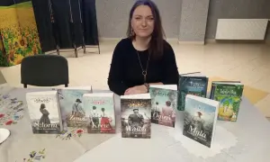 Kobieta prezentuje serię książek "Saga Kaszubska". Na stole widać tytuły: Sztorm, Zemsta, Krew, Walka, Ogień, Mgła, Franc i Walerka.