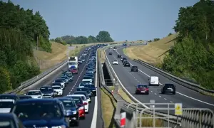 Długi korek samochodów na autostradzie A6. Wiele pojazdów stoi w powolnym ruchu, otoczonych zielenią drzew.