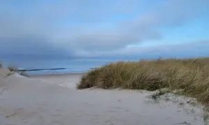 Piasek i trawy na wydmach w Lubiatowie-Kopalinie, z widokiem na spokojne morze i błękitne niebo z chmurami.