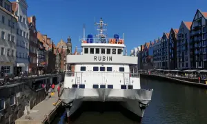 Biały prom "Rubin" cumuje w Gdańsku, gotowy do rejsu na Hel. W tle malownicza starówka i kanał.