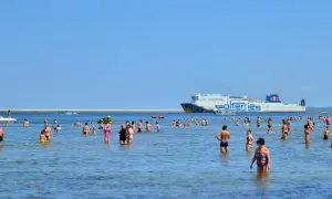 Ludzie kąpią się w morzu, a w tle płynie prom do Ystad.