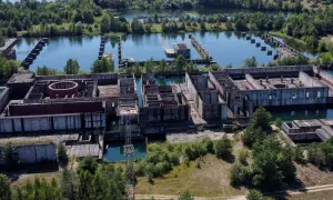 Niedokończona elektrownia w Żarnowcu, z betonowymi konstrukcjami i basenami wypełnionymi wodą, otoczona zielenią.