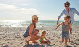 Rodzina cieszy się wakacjami gdzie nad morze z dzieckiem. Mama z tatą obserwują bawiące się maluchy na piaszczystej plaży.