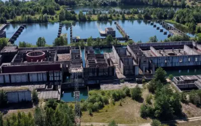 Niedokończona elektrownia w Żarnowcu, z betonowymi konstrukcjami i basenami wypełnionymi wodą, otoczona zielenią.