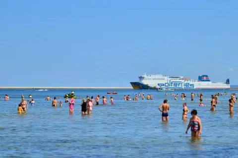 Ludzie kąpią się w morzu, a w tle płynie prom do Ystad.