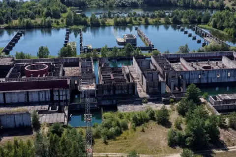 Niedokończona elektrownia w Żarnowcu, z betonowymi konstrukcjami i basenami wypełnionymi wodą, otoczona zielenią.