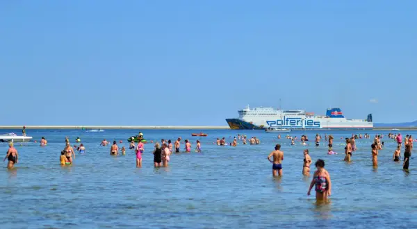 Ludzie kąpią się w morzu, a w tle płynie prom do Ystad.