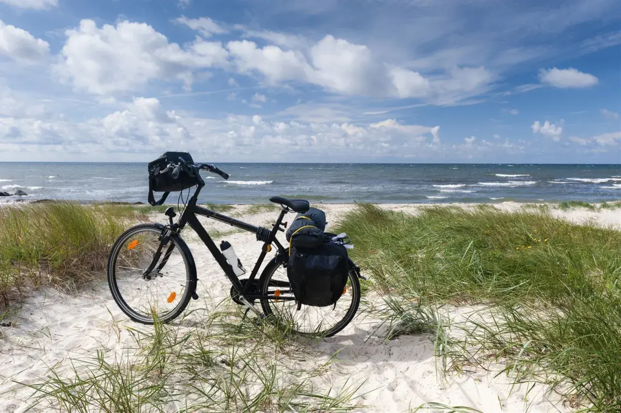 Czarny rower z sakwami na plaży, gotowy do podróży trasą rowerową R10. Morze i niebo w tle.