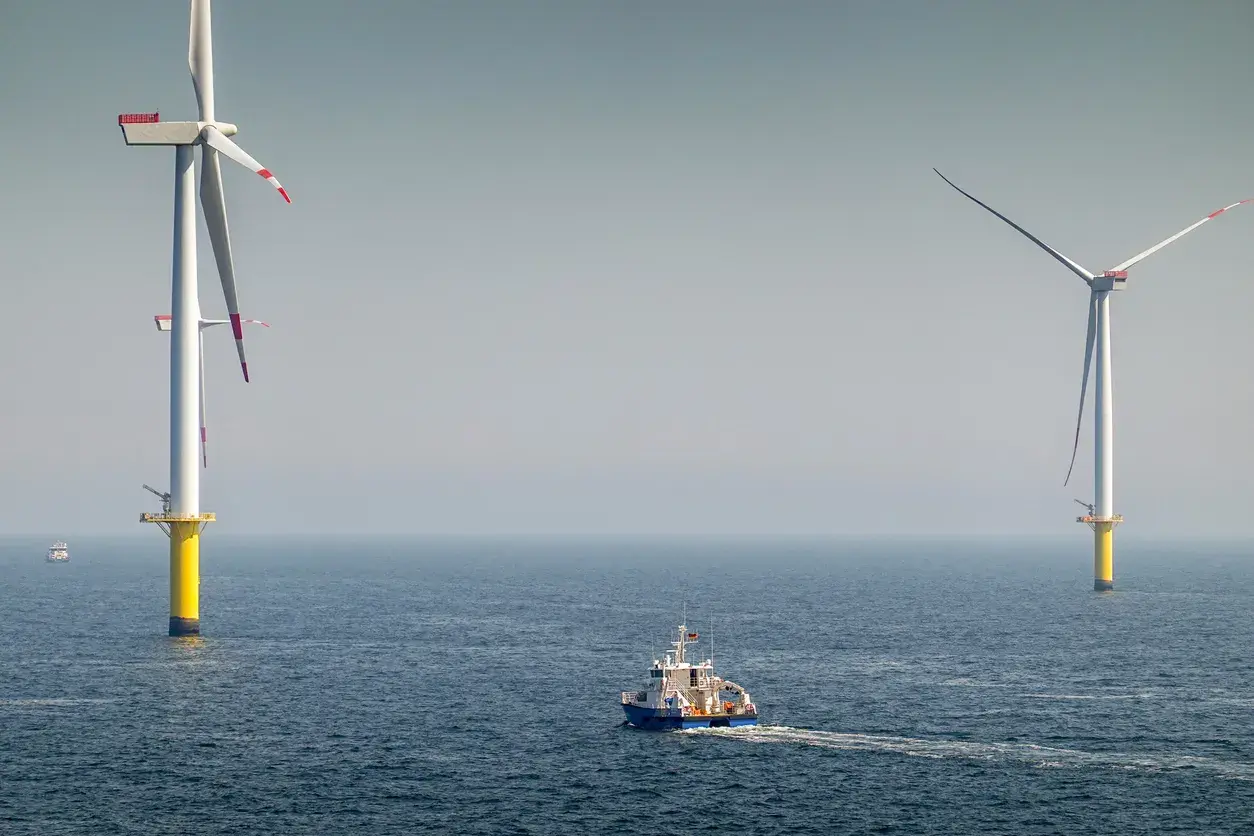 Ogromne turbiny wiatrowe na morzu, symbol nowoczesnej morskiej energetyki wiatrowej, na tle spokojnego oceanu. Statek serwisowy płynie w kierunku jednej z nich.