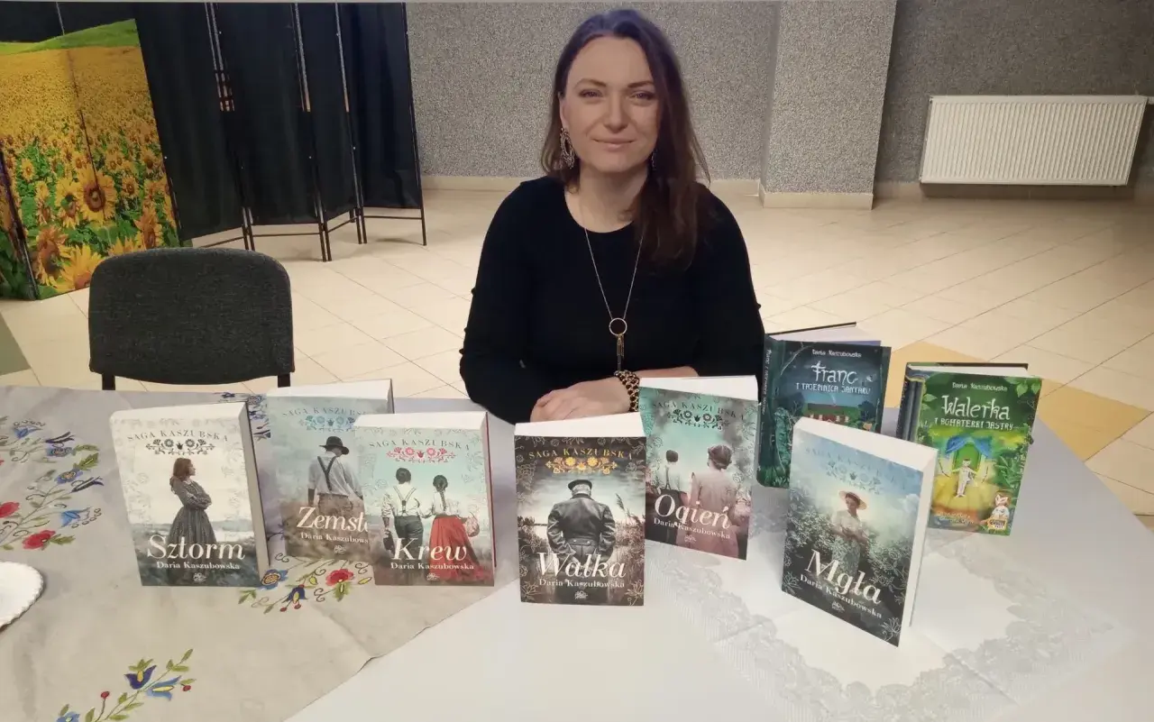 Kobieta prezentuje serię książek "Saga Kaszubska". Na stole widać tytuły: Sztorm, Zemsta, Krew, Walka, Ogień, Mgła, Franc i Walerka.