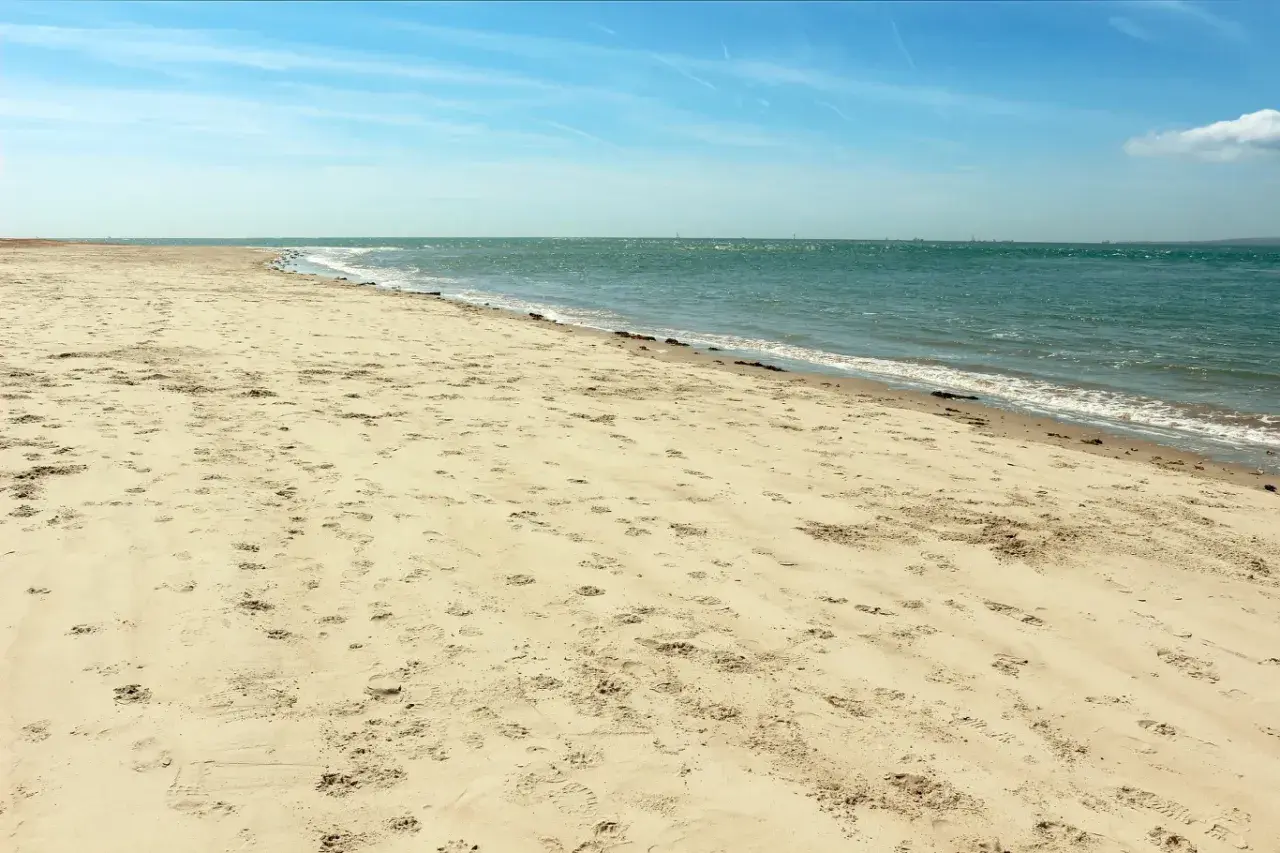 Plaża Ulinia wita piaskiem usianym śladami stóp i spokojnym morzem.