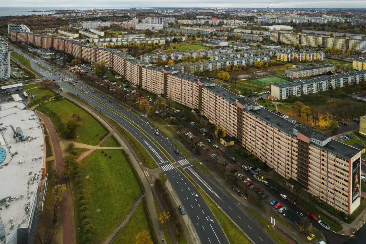Długi, falisty budynek mieszkalny, znany jako falowiec gdańsk, rozciąga się wzdłuż ruchliwej drogi.