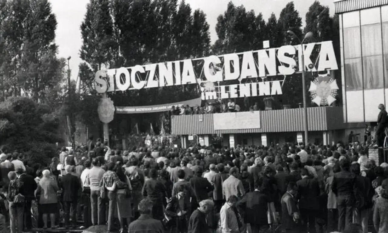 Tłum ludzi zgromadzony przed budynkiem z napisem