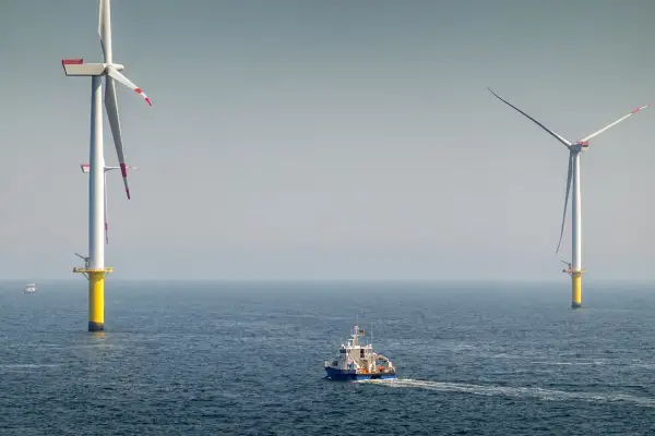 Ogromne turbiny wiatrowe na morzu, symbol nowoczesnej morskiej energetyki wiatrowej, na tle spokojnego oceanu. Statek serwisowy płynie w kierunku jednej z nich.