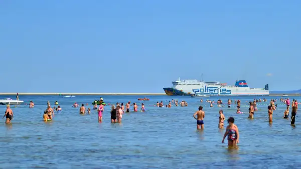 Ludzie kąpią się w morzu, a w tle płynie prom do Ystad.
