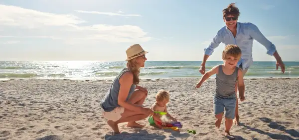 Rodzina cieszy się wakacjami gdzie nad morze z dzieckiem. Mama z tatą obserwują bawiące się maluchy na piaszczystej plaży.