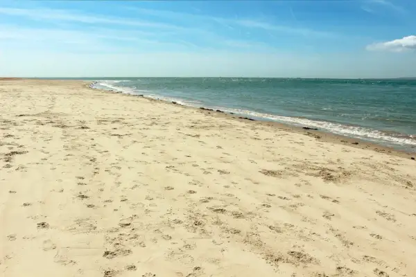 Plaża Ulinia wita piaskiem usianym śladami stóp i spokojnym morzem.