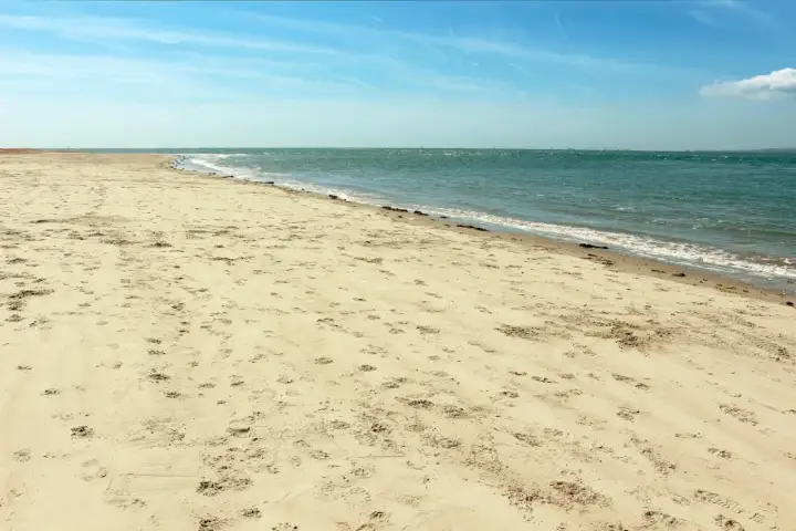 Plaża Ulinia wita piaskiem usianym śladami stóp i spokojnym morzem.